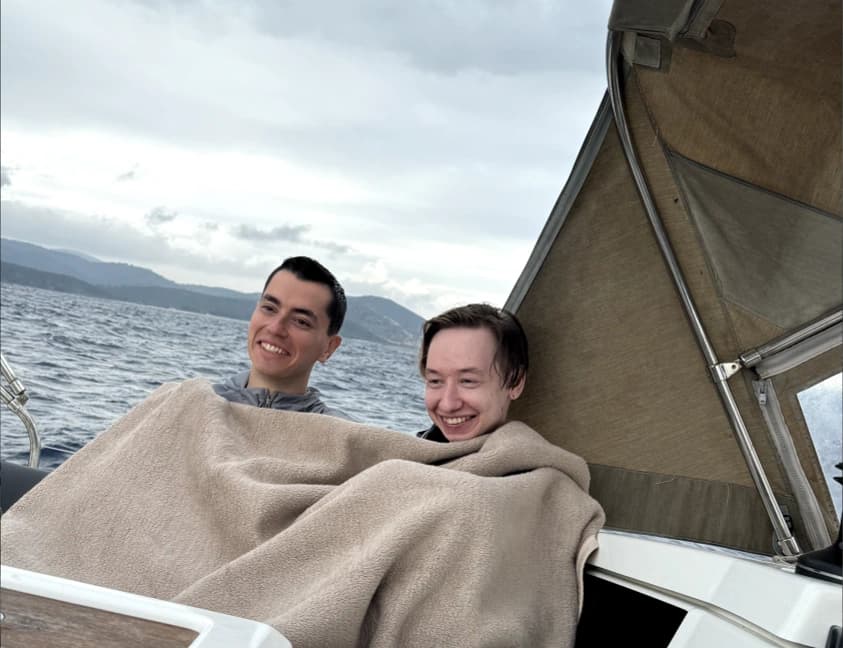 Two people wrapped in a blanket on board a boat