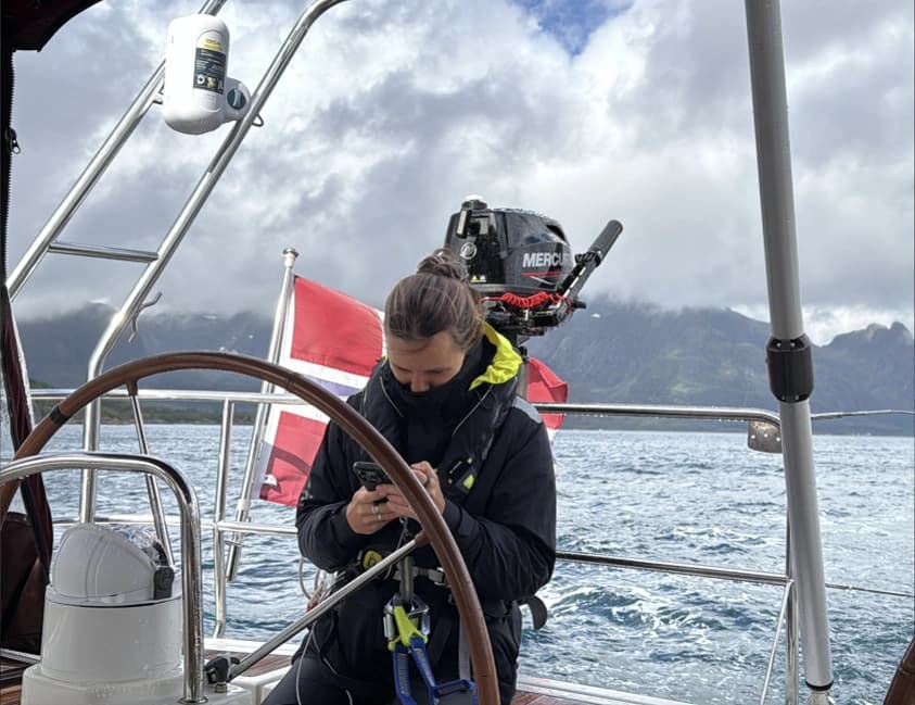 A woman wearing a life jacket beside the wheel of a sailing yacht