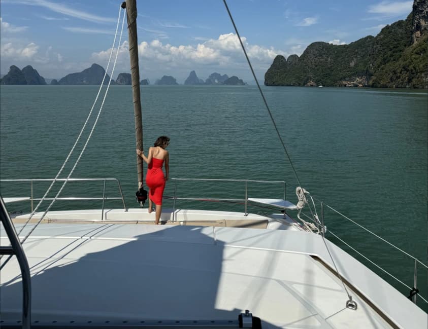 A woman standing at the bow of a catamaran in a tropical bay